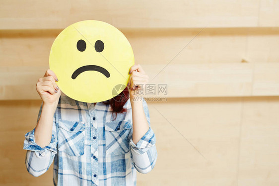 身穿便装面戴悲伤面具站在木墙边遮面的年轻女子的Waist图片