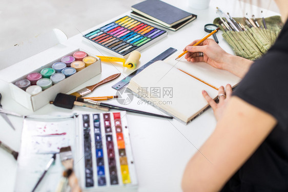 在艺术工作室的素描本中使用铅笔粉彩颜料和画笔创作新图片的艺术图片