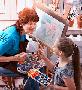 艺术家在工作室画架正宗的老妇人和孩子女孩用调色板水彩颜料调色板和刷子早晨的阳光私人企业绘图图片