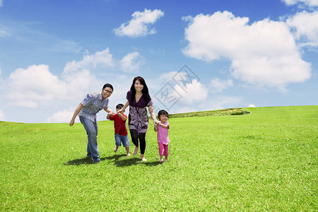 亚裔父母带着孩子在草地上行走天空背景美丽图片