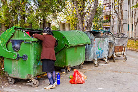 无家可归的女人正在垃圾箱里寻找食物贫穷的女人正在寻找图片