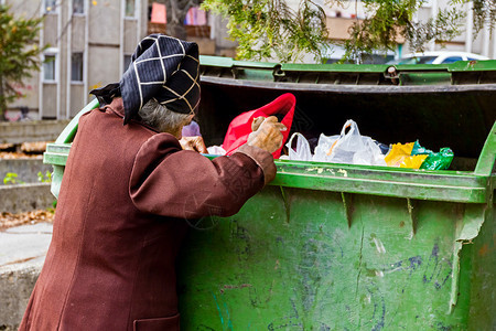 无家可归的女人正在垃圾箱里寻找食物贫穷的女人正在寻找图片