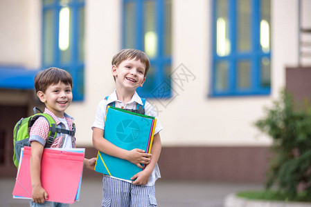 可爱的小学生在校园里轻快地交谈孩子们的心情很好温暖的春天早晨在同学的书包背后在其中一个男孩鲜红色背景图片