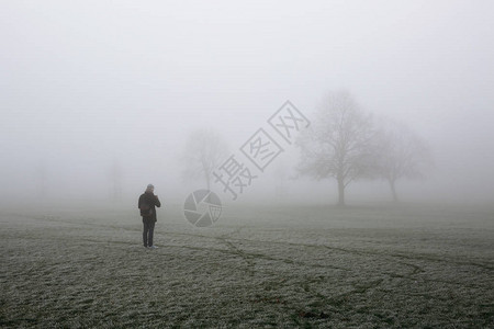 身着冬衣的年轻人带着手机拍照在伦敦布罗姆菲尔德公园在寒冬清晨在雾中图片