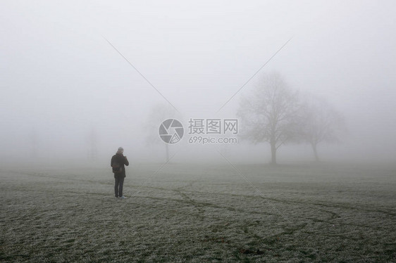 身着冬衣的年轻人带着手机拍照在伦敦布罗姆菲尔德公园在寒冬清晨在雾中图片