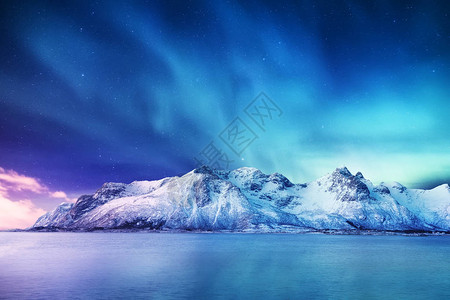 挪威罗弗敦群岛上的北极光山上的绿色北极光夜间冬季景观与极光和水面上的反图片