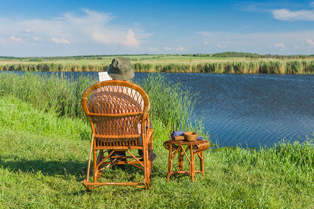 夏季老人坐在河边的柳条摇椅上看书图片