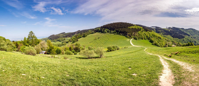 春天风景的全景与土路穿过绿色草甸和蓝天白云捷克图片