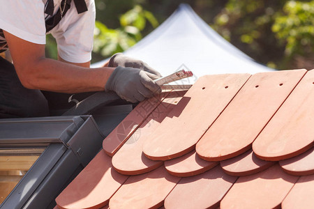 别墅屋顶自然屋顶瓷砖的坚硬Roofer建筑工人使用ruller测量瓷背景