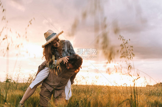 快乐的男人在夏日草地上背着他的女朋友图片