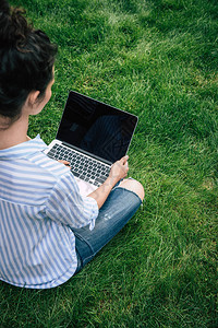 用笔记本电脑在坐草地上时用空白屏幕的笔记本电脑对褐色图片