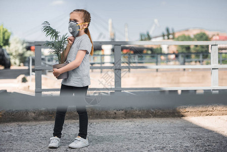 戴防护面具的儿童携带绿色盆栽图片