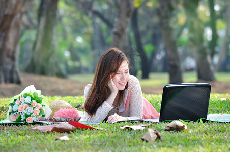 妇女坐在木垫上在公园里看笔记本电脑背景图片