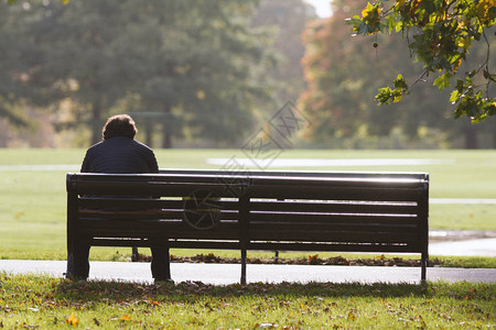 在秋天公园的孤独男子坐在长椅上图片