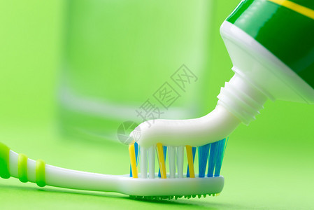 在绿色背景的牙刷上挤压牙膏的特写图片