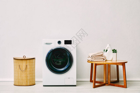洗衣篮附近的现代洗衣机带毛巾的咖啡桌洗涤剂瓶图片