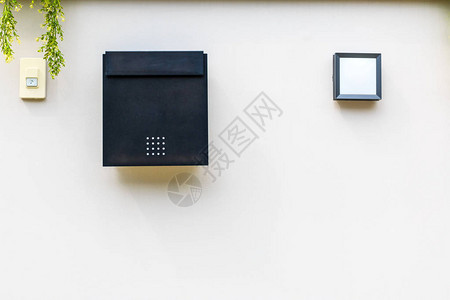 一个带有灯箱和门铃开关的黑色邮筒在白墙上图片