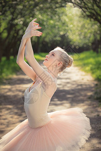 穿着白色芭蕾舞短裙在绿色景观中跳舞的完美身材的年轻女子美丽的芭蕾舞女演员展示经典芭蕾姿势女柔情背景图片