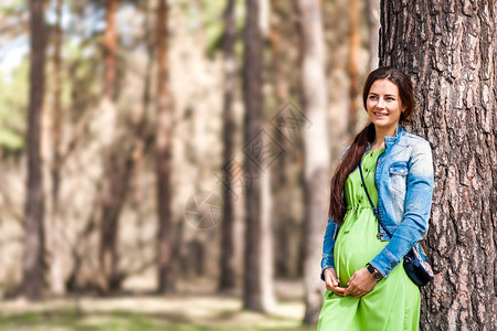 一个年轻时尚的孕妇带着微笑和双手放在她的肚子上在夏天散步一个孕妇图片