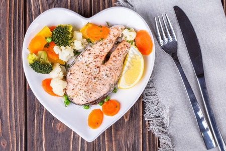 蒸鲑鱼和盘子里的蔬菜以木本底心脏形式图片