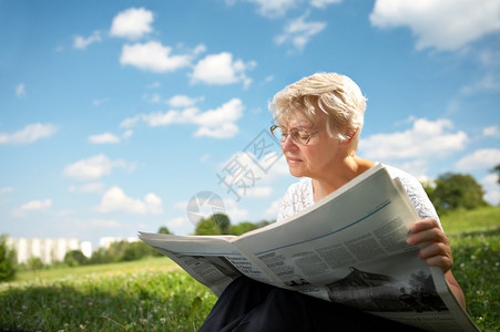 这名年老妇女坐在公园的草地上图片