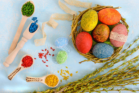 以浅背景和多彩大米作为装饰绘画的柳木树巢中的彩色鸡蛋图片