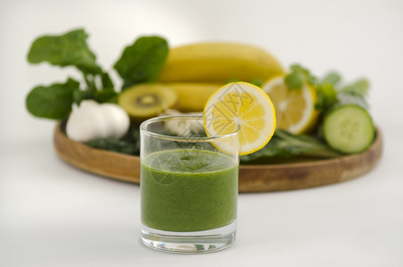 绿色冰沙碱饮食料与新鲜柠檬旁边的木制托盘与碱饮食蔬菜和水果图片
