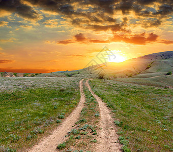 日落背景山中绿色草地上的道路图片