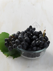 白色木制背景透明碗中的黑葡萄图片