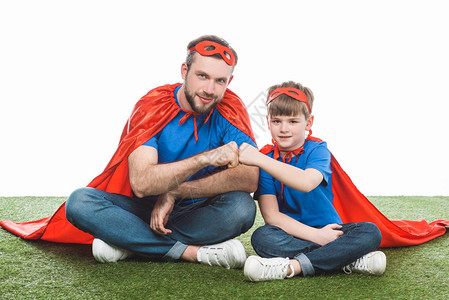 父亲和儿子穿着超级英雄服装坐在草坪上图片