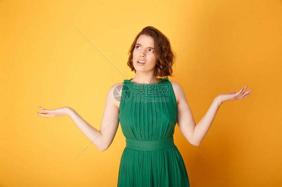 用橙色隔离的双臂张开的困惑女人的肖像图片