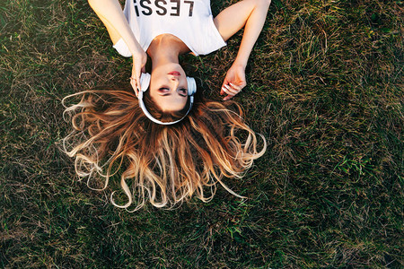 坐在草坪上用耳机收听音乐闭着眼睛的年轻美女身着散装便图片