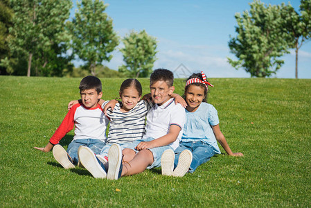 坐在绿色草地上笑着微笑的可爱多种族儿童图片