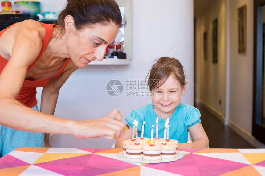 三岁的金发孩子微笑着看女人在家里用打火机在生日蛋糕上点燃蜡烛图片