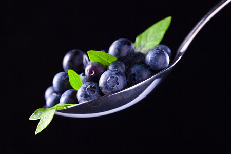 黑色背景上的蓝莓成熟浆果和绿叶图片