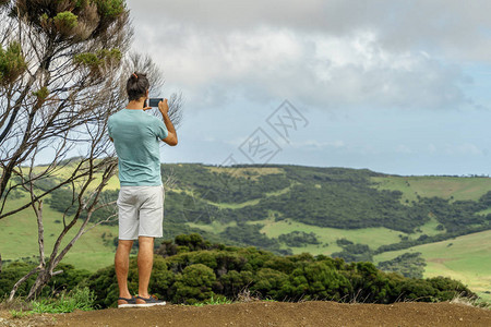 人类用智能手机拍摄美丽的绿色山谷照片的后方图片