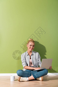 穿着笔记本电脑坐在地板上靠着绿色墙壁图片