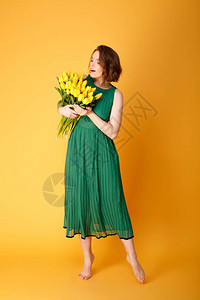 穿着绿春装的漂亮女人看着黄色郁金香花束在橙色与图片