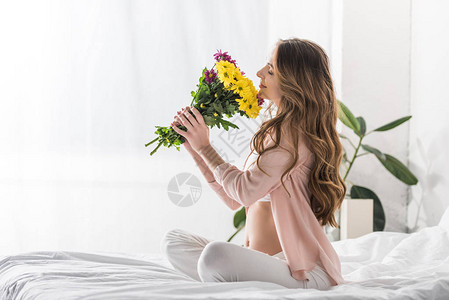 美丽的孕妇坐在床上闻花香躺在背景图片