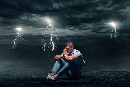 年轻人坐在沙漠的地上暴风雨背图片