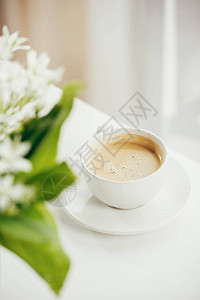 在白色桌面上放着一束鲜花的咖啡杯特写背景图片