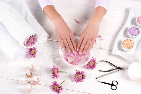 女在餐桌上用鲜花毛巾五颜六色的海盐芳香油瓶指甲油奶油容器和美容院修指甲工具接受指甲图片