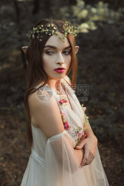 身着花裙和花圈的美丽的女精灵在森林中与图片