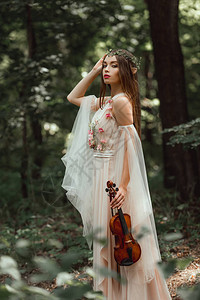 穿着花裙子和花环的神秘精灵在森林里拿着小提琴图片