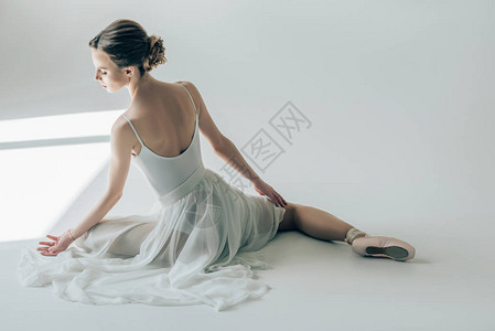 芭蕾舞女演员坐在白色礼服和芭蕾舞鞋的后视图图片