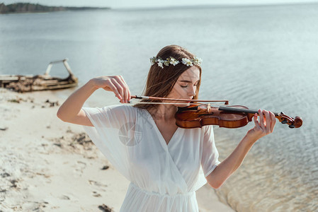 穿着优雅礼服和花圈在海边拉小提琴的图片