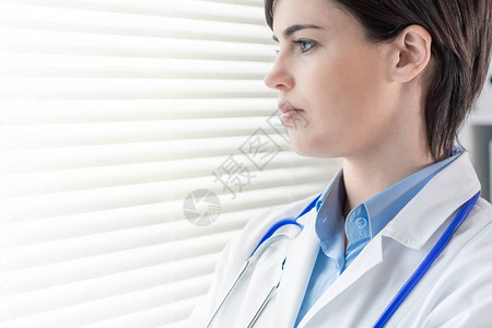 有吸引力的体贴的年轻女医生或护士站在高调的窗户外面背景图片