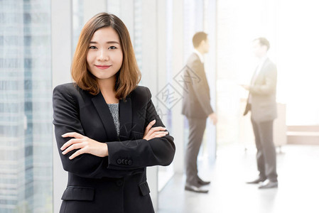在办公大楼走廊站立和越过她的手臂的亚洲女自信女商心安图片
