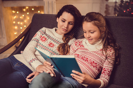 母亲和女儿在圣诞节晚上一起睡沙发时读书图片