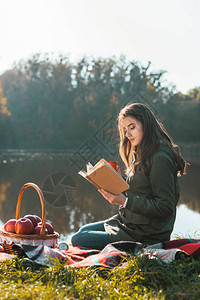 在公园池塘附近的毯子上看到有咖啡杯阅读书的迷人年图片